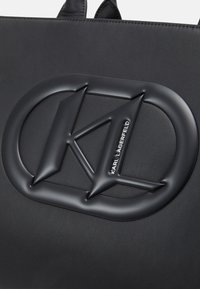 Surface en cuir noir embossée avec un logo Karl Lagerfeld en relief, présentant des lettres stylisées "KL" dans un cadre ovale.