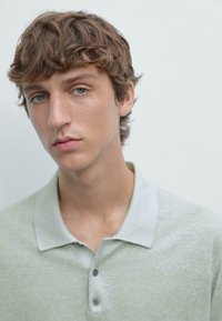 Světle zelená polokošile s límcem, vyrobená z texturované tkaniny, se šedým kontrastním límcem a dvěma tmavými knoflíky na léze.