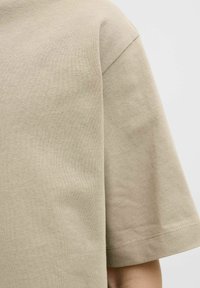 Beige Baumwoll-T-Shirt mit kurzen Ärmeln, Rundhalsausschnitt und subtiler Textur mit glatter Oberfläche.