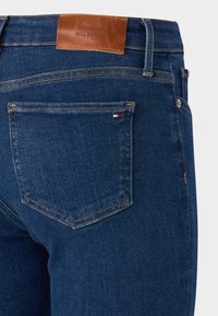 Mørkeblå denimjeans med et lærlogo-patch, fem-lomme design, oransje søm og et lite stripete aksent på baklommen.