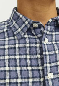 Cămașă flanel cu carouri, în culori albastre și albe, având guler cu button-down și butoane albe. Textură moale și material cald.