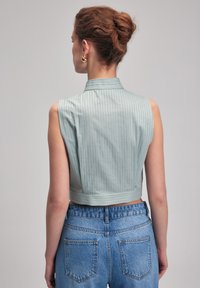 Top recortado sin mangas en tela de rayas azul claro, con un cuello estructurado y una cintura ajustada, acompañado de jeans de mezclilla de tiro alto.