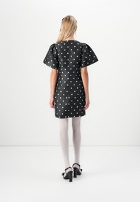 Zwart jurkje met stippen, korte puffmouwen, een gladde textuur en een getailleerde silhoutte. Gemaakt met lichte panty's en zwarte hakken met strikken.