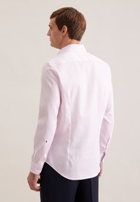 Camicia a maniche lunghe di colore rosa chiaro con colletto appuntito, taglio su misura e polsini con bottoni decorati da un piccolo ricamo. Tessuto dalla texture liscia.