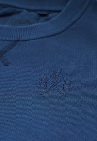 Marinblå sweatshirt med ribbat krage, med en diskret präglad logotyp i matchande ton. Mjuk textur och en klassisk, enkel design.