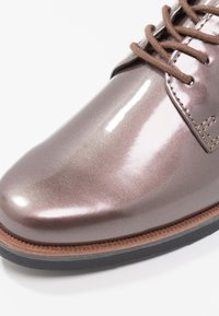 Chaussure Oxford métallique marron avec une finition brillante, dotée de lacets marron et d'une semelle texturée avec une bordure contrastante marron clair.