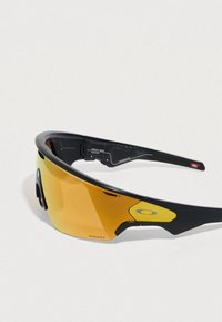 Sport sunglasses with a black frame, yellow-tinted lens, aerodynamic design, and a prominent logo on the side. Lightweight and sporty.