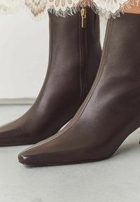 Bruine leren enkelboordels met een spitse neus, voorzien van een zijrits en een klein hakje. Gladde textuur en strak ontwerp.