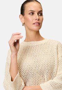 Light beige knitted sweater with a loose, open weave pattern and ribbed cuffs. Features a round neckline and three-quarter sleeves.