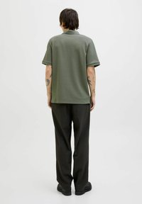 Polo shirt verde oliva con maniche corte e finitura texture, abbinato a pantaloni scuri e scarpe nere; vista posteriore.