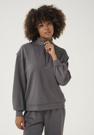 Maglione grigio con collo a metà zip, spalle scese e maniche a polsino. Tessuto morbido e vestibilità rilassata. Abbinato a pantaloni coordinati.