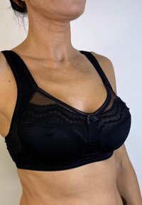 Sujeción negra con aros, fabricada con tejido texturizado, detalles de malla y acabado de encaje; cuenta con tirantes anchos y un lazo central como acento.