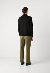 Pulover negru tricotat, asortat cu pantaloni verzi măslin, având o croială relaxată și manșete standard. Culoare uniformă, fără modele sau accente vizibile.