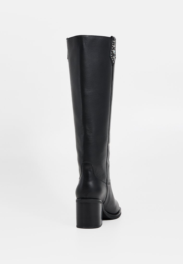 Botte noire en cuir montante, avec un bout rond, un talon carré et des accents cloutés sur le côté. Texture lisse et design minimaliste.