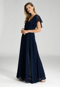 Abito maxi blu navy in tessuto leggero con maniche a volant, scollatura a V e gonna fluida. Presenta una vita aderente e dettagli trasparenti.