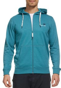 Haut de sweatshirt zippé en teal avec une capuche à cordon de serrage, des poches avant et un logo brodé. Le tissu semble doux avec une finition texturée.