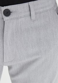 Ljust grå byxor med en texturerad väv, med en svart knapp i midjan och en platt frontdesign.