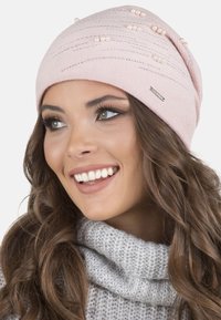 Gorro de punto rosa con adornos de perlas y strass, que presenta un ajuste ceñido y un sutil patrón texturizado. Detalles de hardware en plata visibles.