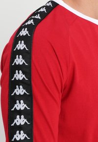 Rode lange mouwen overhemd met een zwart zijpaneel met herhaaldelijk wit logo-ontwerp. Zachte stof met een ronde hals.