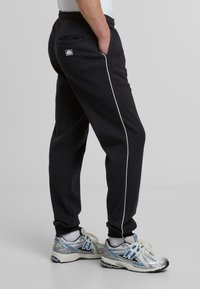 Svart joggebukser med hvite detaljer, elastisk midje, sidelommer og tapering design. Kombinert med sølv- og blå joggesko.