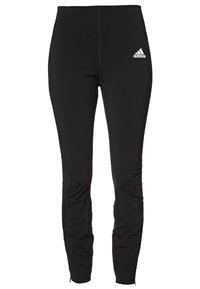 Czarne sportowe spodnie z elastycznego materiału, o smukłym kroju, z kontrastowymi szwami, kieszeniami na zamek i logo Adidas na biodrze.