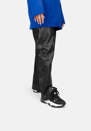Pantaloni in pelle nera con una texture liscia, caratterizzati da cuciture e una vestibilità comoda. Abbinati a sneakere chunky in bianco e nero. Giacca oversized blu.