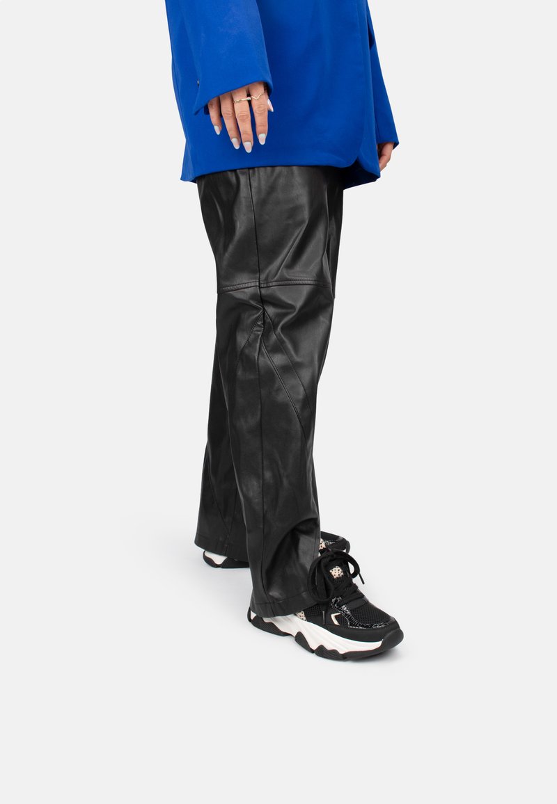 Schwarze Lederhosen mit glatter Textur, mit Nähten und einer lässigen Passform. Kombiniert mit schwarz-weißen, klobigen Sneakers. Blauer übergroßer Jacke.