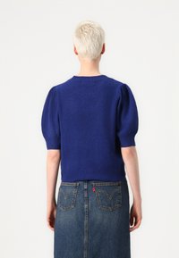 Pull en tricot bleu marine à manches courtes avec des manches bouffantes, col rond et ourlet ajusté, associé à une jupe en denim avec des poches arrière.