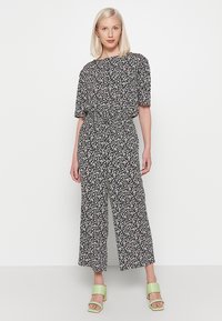 Zwarte bloemenoverall met korte mouwen, relaxte pasvorm, elastische taille en wijde pijpen. Het patroon heeft kleine witte en roze bloemen.