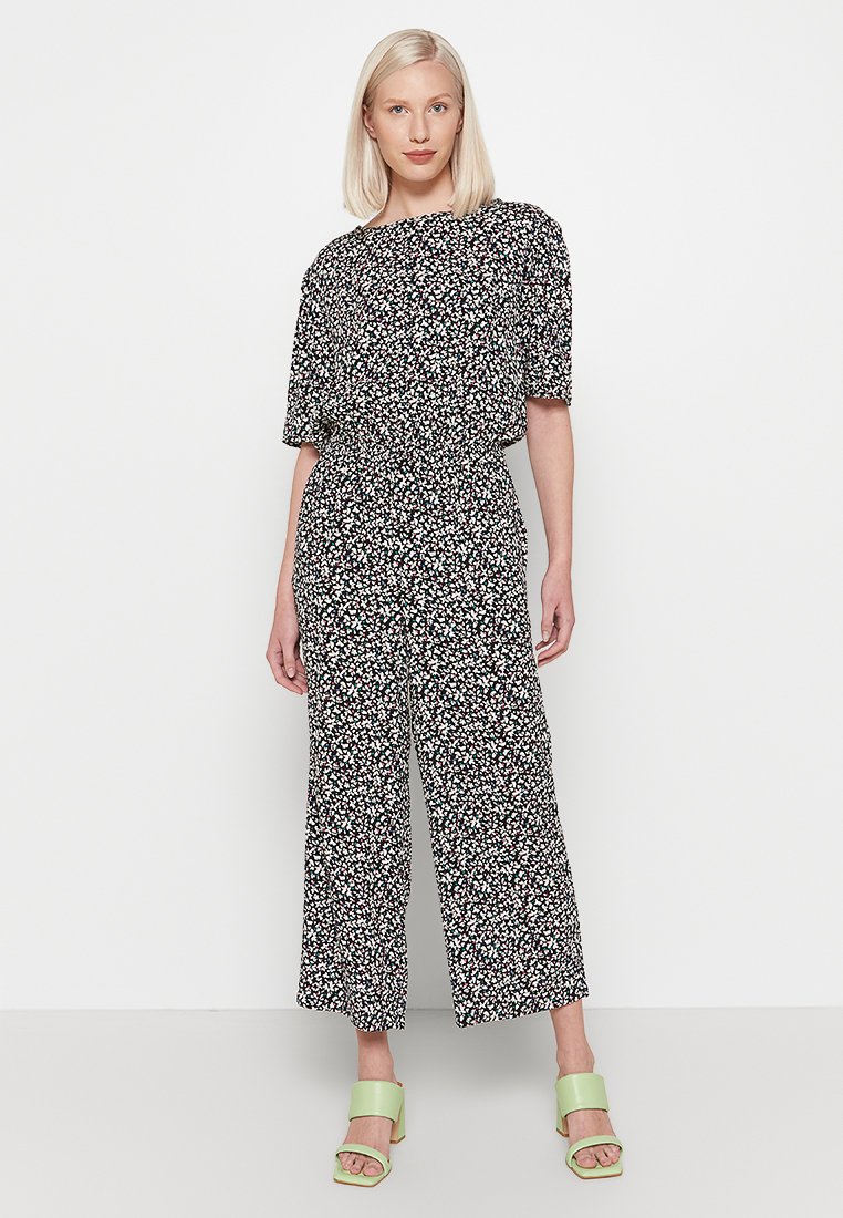 Zwarte bloemenoverall met korte mouwen, relaxte pasvorm, elastische taille en wijde pijpen. Het patroon heeft kleine witte en roze bloemen.