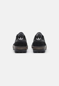 Zapatillas deportivas negras con parte superior de ante, suela de goma y cuello acolchado. Presenta un logo icónico en el talón y detalles texturizados.