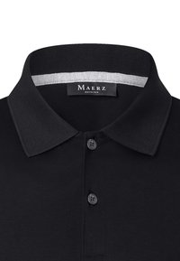 Svart polo-t-shirt med två knappar, ribbad krage och inneretikett med texten "Maerz Muenchen."