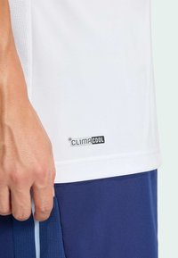 Witte sportieve shirt met korte mouwen en mesh zijpanelen, voorzien van zwarte "CLIMACOOL" branding. De stof lijkt lichtgewicht en ademend.