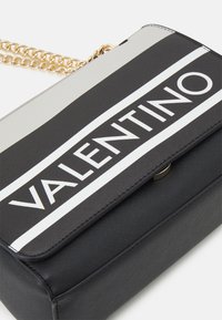 Černá a šedá taška s řetízkovým popruhem, s texturovaným povrchem a odvážným logem "VALENTINO" na pruhovaném pozadí.