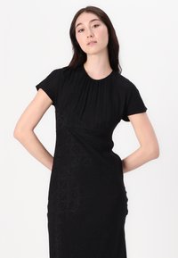 Black dress with short sleeves, featuring a pleated neckline and subtle textured pattern. Smooth fabric with a fitted silhouette.