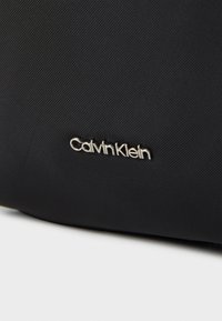 Černá nylonová taška s stříbrným logem Calvin Klein. Texturovaný materiál a čisté linie zdůrazňují její moderní design.