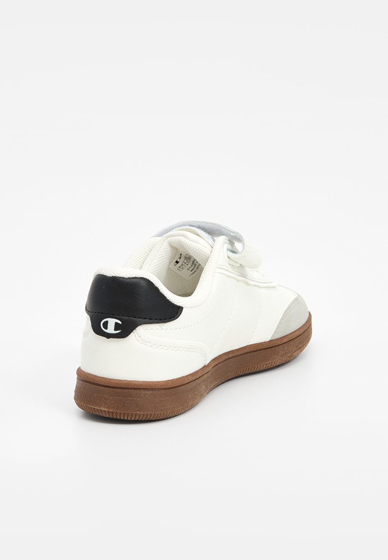 Zapatilla blanca con talón negro y acentos grises. Parte superior de sintético suave, punta redondeada y suela de goma marrón texturizada. Cierre de Velcro.