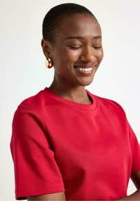 Rødt kortærmet T-shirt lavet af glat stof med rund hals. Har en afslappet pasform og synlige sømme på ærmerne.