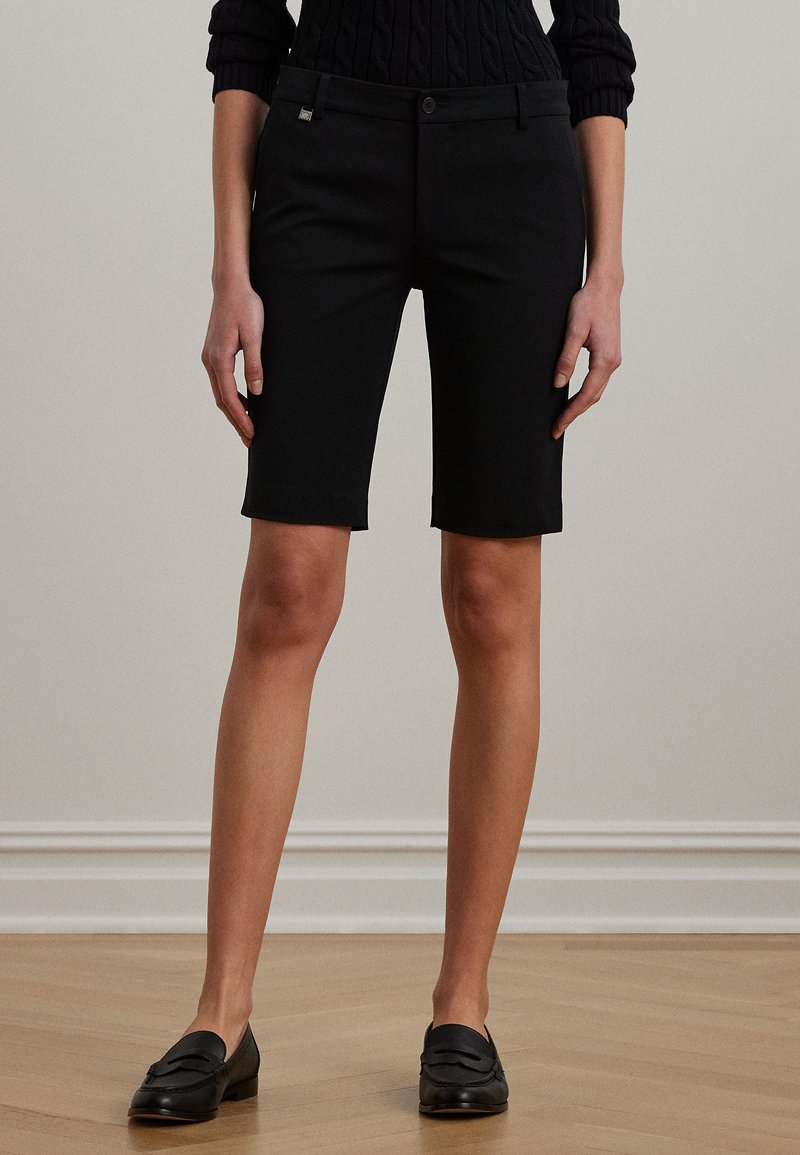 Melnas, piegrieztas bermudu šorti no strukturētas auduma. Ar priekšējo pogu aizdari, jostas cilpām un šauru pieguļošu siluetu, kas sniedzas līdz vidus augšstilbam.