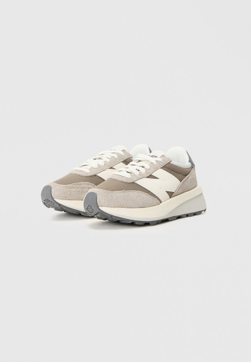 Beige und graue Sportschuhe mit einem Obermaterial aus Stoff, strukturierten Akzenten, weißem Logodetail, flachen Schnürsenkeln und einer dicken Gummisohle.