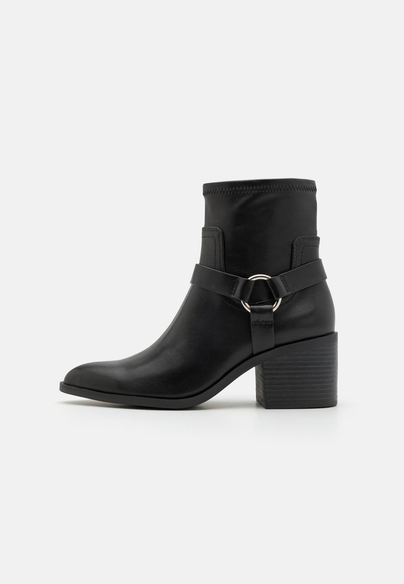 Black leather ankle boot with a rounded toe, a wide block heel, a fabric cuff, and a buckle strap detail with a circular accent.