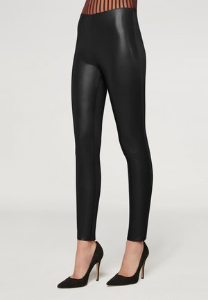 Leggings neri realizzati in un materiale lucido, con un design aderente e pannelli laterali. Abbinati a scarpe con tacco alto nere.