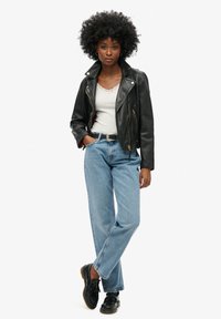 Chaqueta de cuero negra de motorista con cremalleras plateadas, llevada sobre una blusa gris con encaje; combinada con jeans de talle alto de color azul claro y zapatos negros.