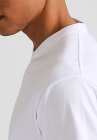 Witte katoenen t-shirt met een v-hals ontwerp. Het heeft een gladde textuur en nette stiksels langs de schouders en de halslijn.
