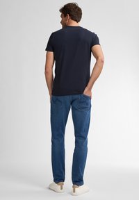 Camiseta de manga corta azul marino combinada con jeans de mezclilla azul. Los jeans tienen bolsillos traseros con costuras sutiles. Calzado son zapatillas deportivas blancas.
