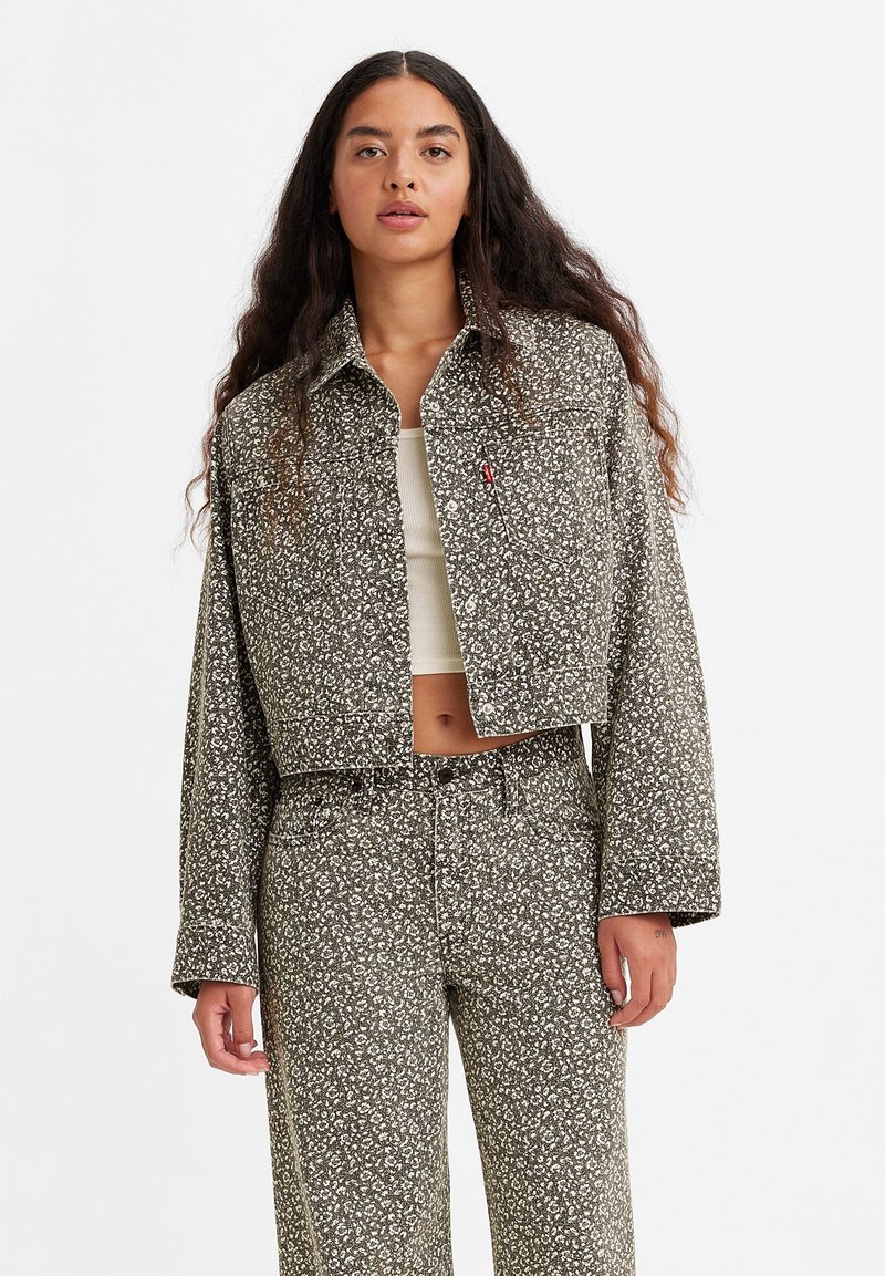 Chaqueta corta de tela estampada en verde oliva con diseños florales en blanco, que presenta un cierre de botones y cuello.
