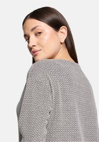 Textureret sweater i sort-hvid strikkemønster, med rund halsudskæring og sænkede skuldre, set fra en let vinkel.