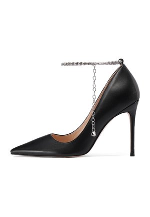 Scarpa nera in pelle con tacco alto e punta affilata, caratterizzata da una sottile catena argentata alla caviglia e un tacco a stiletto.