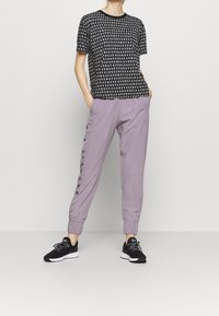 Camiseta negra con letras blancas, combinada con pantalones deportivos lavanda que tienen bolsillos laterales y puños en los tobillos. Zapatillas deportivas negras.