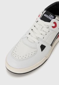 Balti odiniai sportbačiai su perforuota nosimi, juodais akcentais, raudonomis akių skylutėmis ir "LOVE MOSCHINO" prekės ženklu. Yra plokščios raištelės ir tekstūruotas padas.